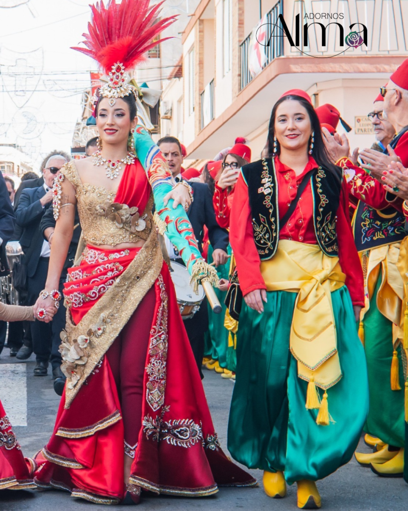Participantes en un desfile de Moros y Cristianos con trajes coloridos y tocados de plumas rojas